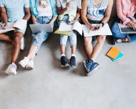 Overhead portrait of young people with laptops and smartphones, sitting together on the floor. Students writing lectures holding textbooks on their knees.
